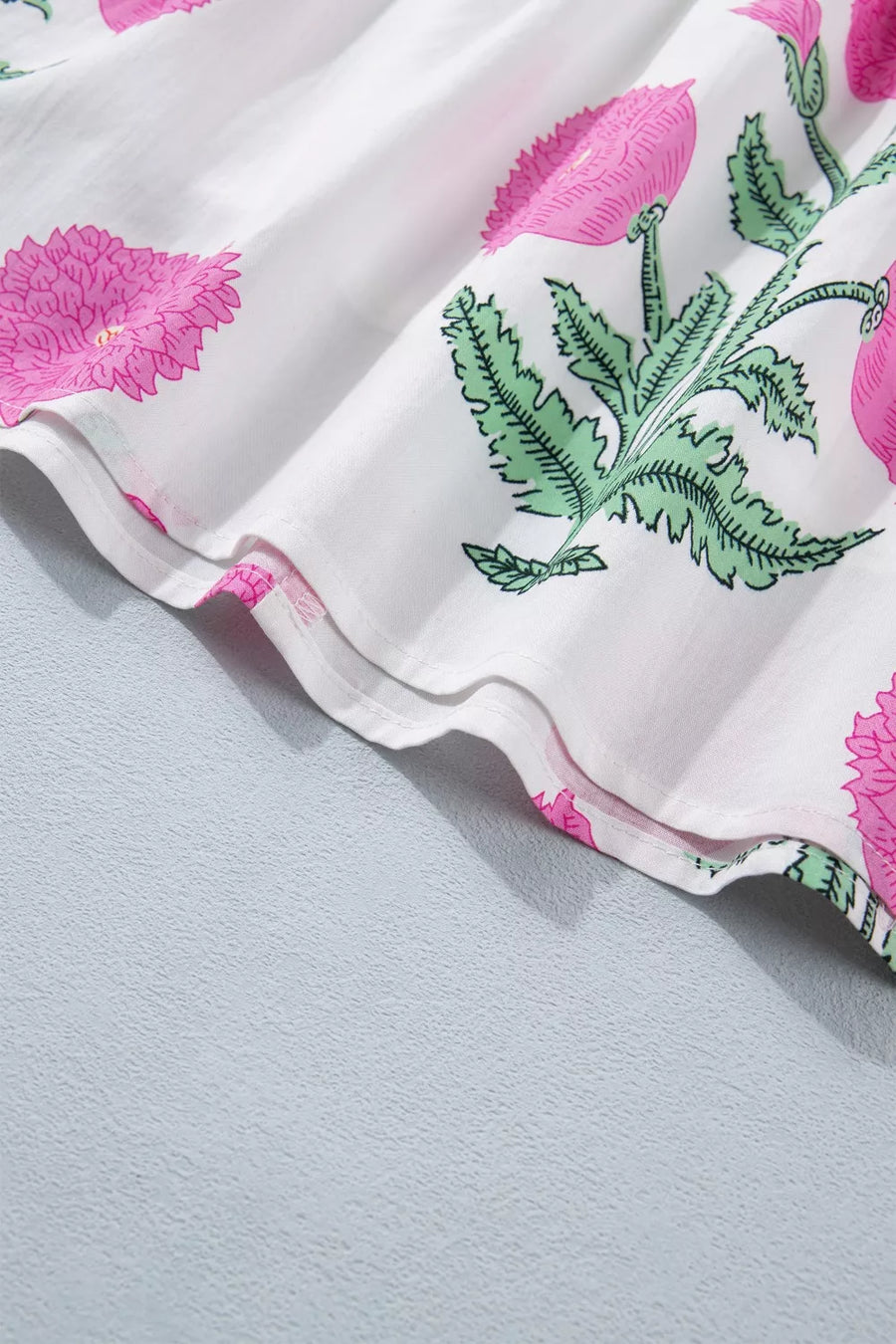 Vibrant floral ruffle mini dress with pink floral print on white fabric, showing ruffled hem detail.
