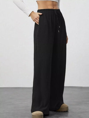 Black ribbed wide-leg pants with drawstring and pockets, styled casually.
