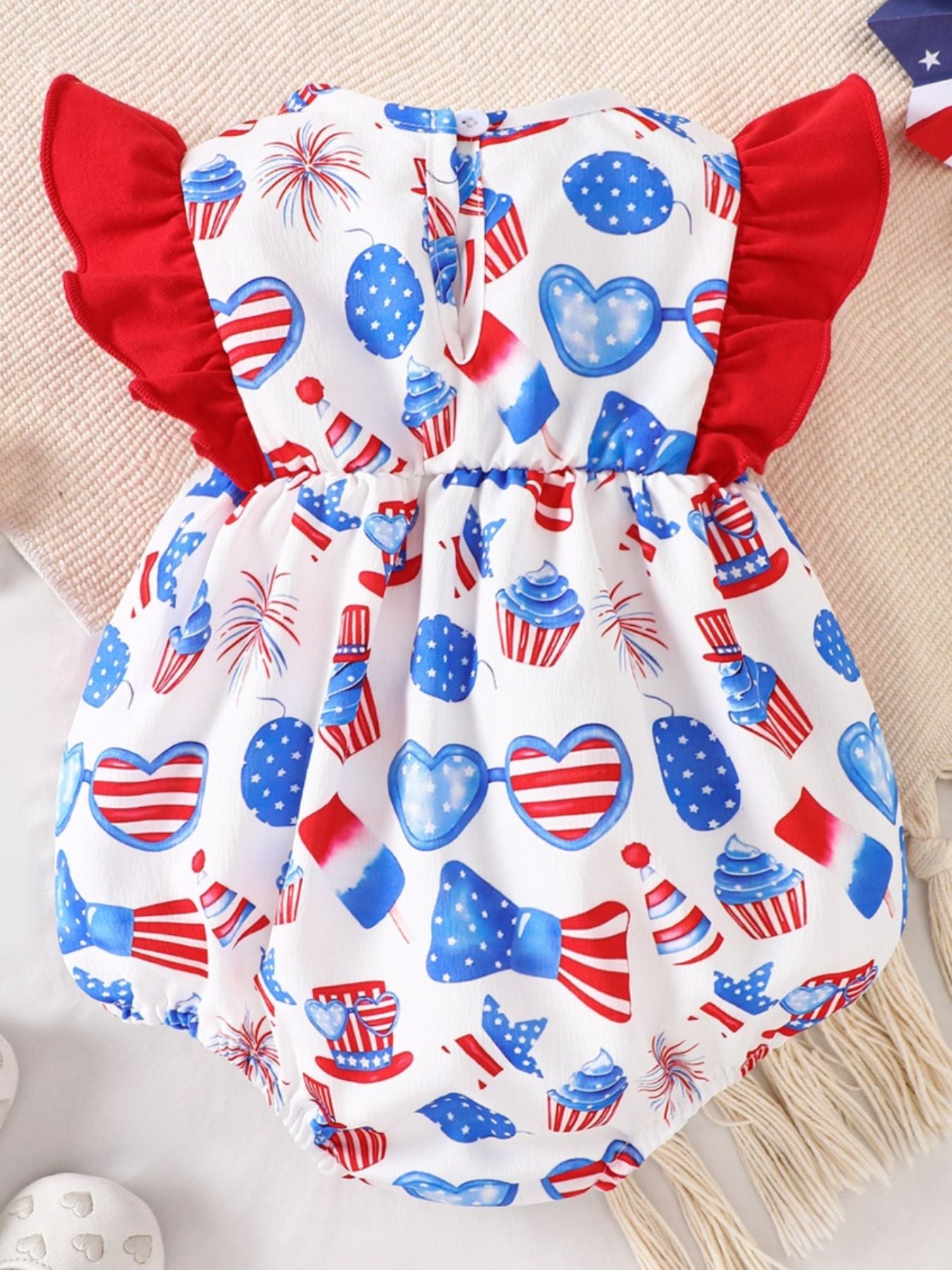 Baby one-piece with patriotic print, red ruffle sleeves, and cupcake and heart sunglasses details.