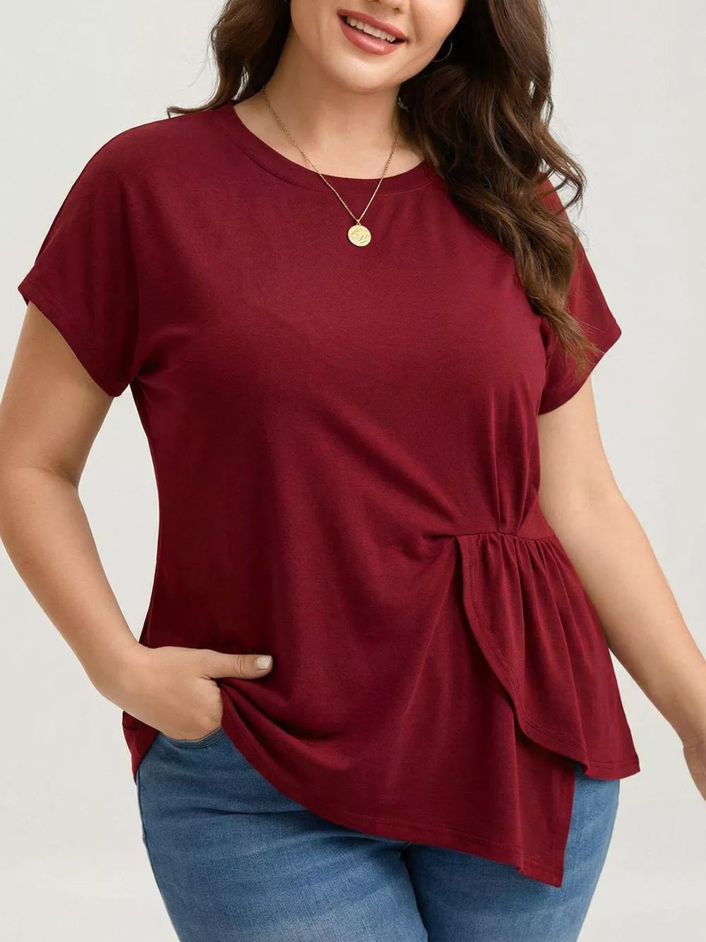 Plus-size burgundy crew neck t-shirt with asymmetrical ruched hem detail.