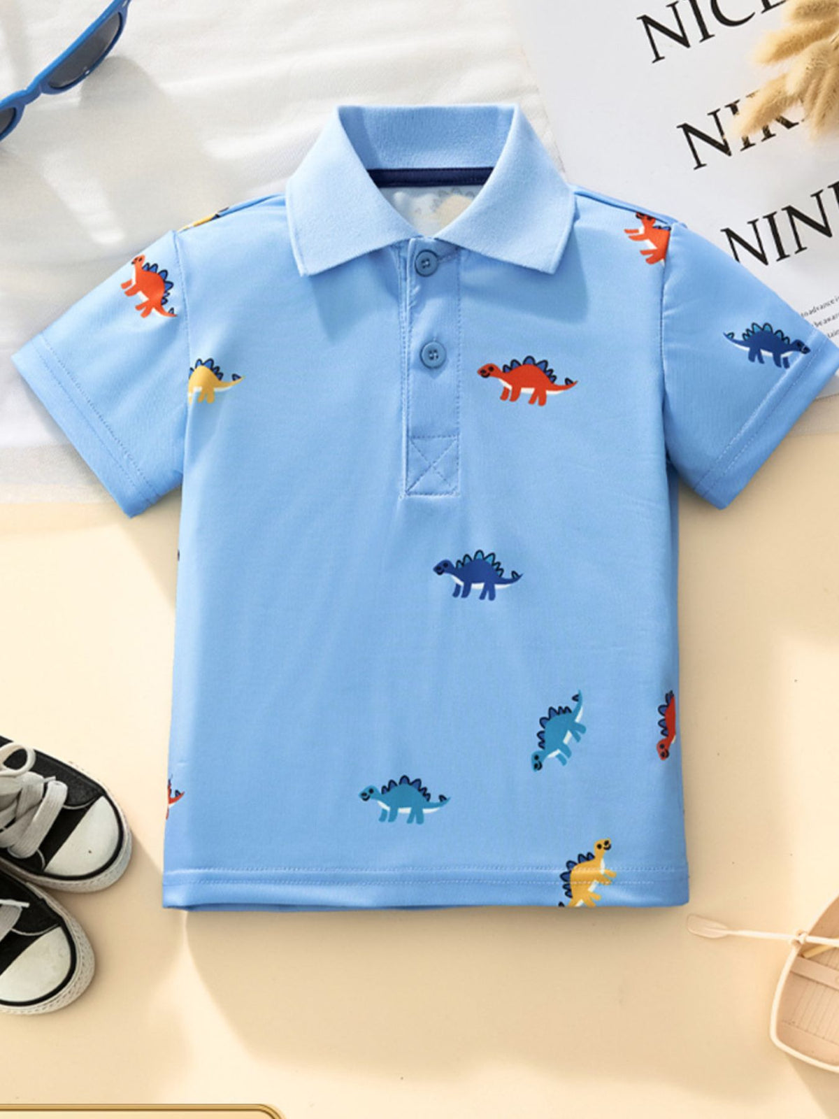 Light blue toddler polo shirt with colorful dinosaur print, short sleeves, and button placket.