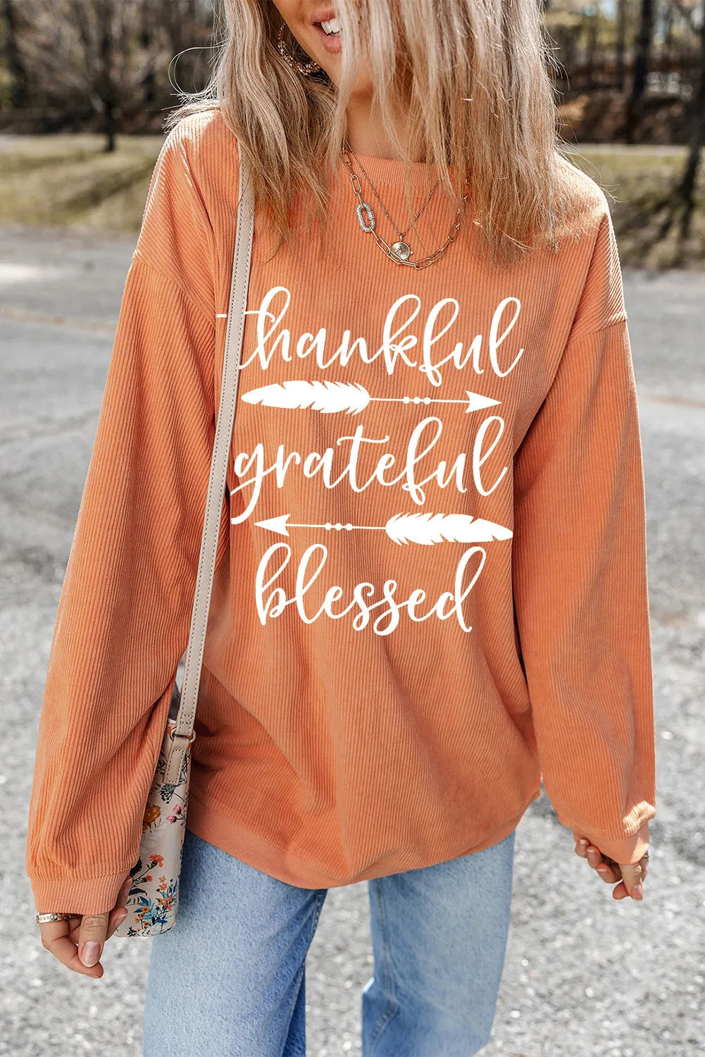 Corduroy crewneck sweatshirt in sherbet with white graphic text and feather accents.