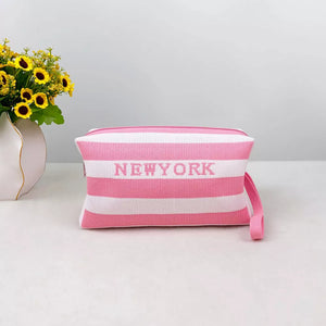 Striped small cosmetic bag in blush pink and white with New York text and wrist strap.