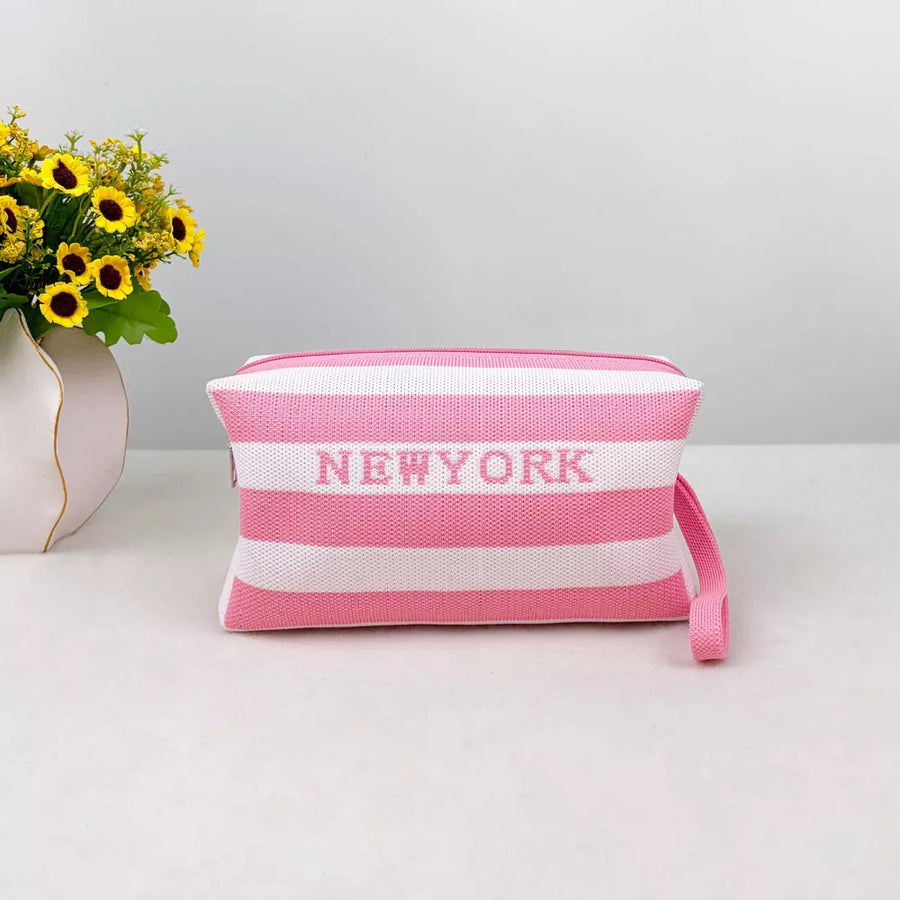 Striped small cosmetic bag in blush pink and white with New York text and wrist strap.