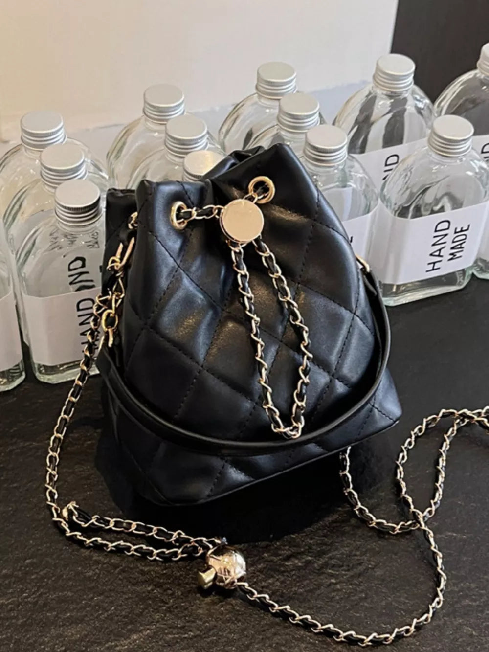Black quilted bucket bag with gold chain strap and drawstring closure.