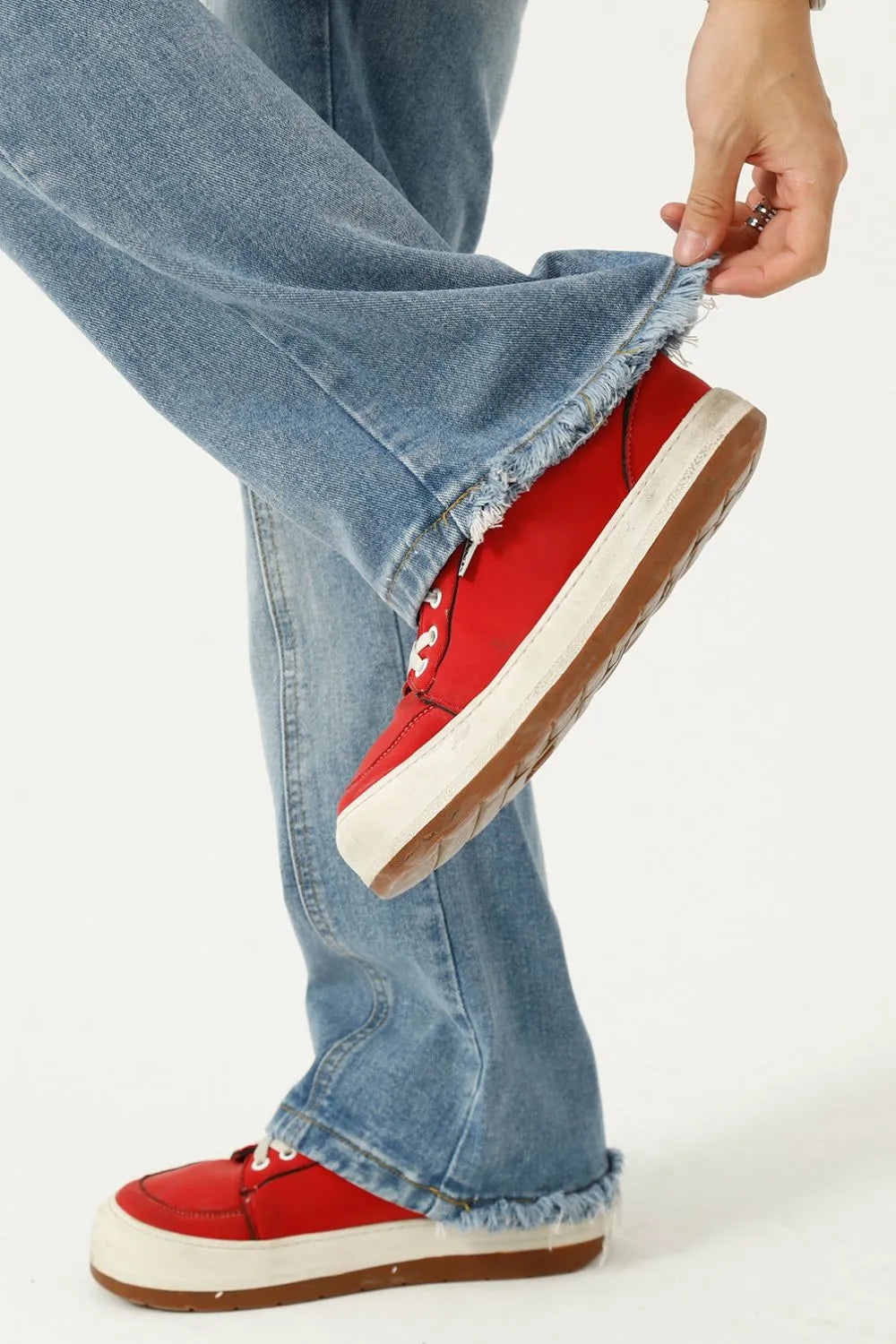 Seam detail flare jeans in medium wash denim with frayed hems styled with red sneakers.
