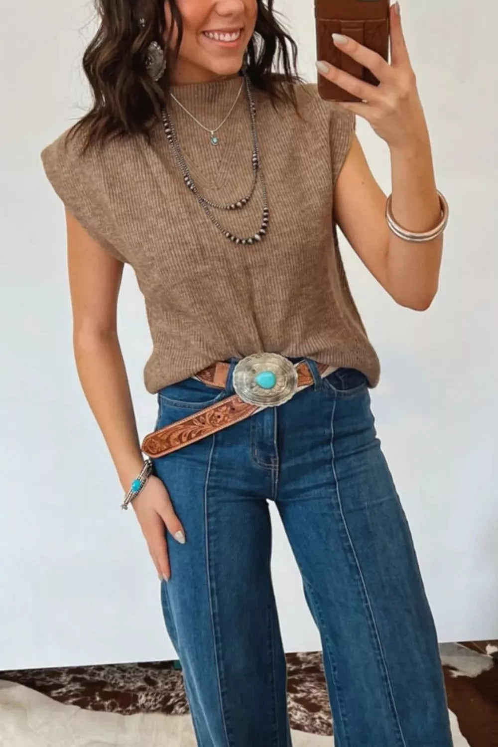 Brown ribbed knit mock neck sweater vest with cap sleeves, styled with jeans and a turquoise belt.