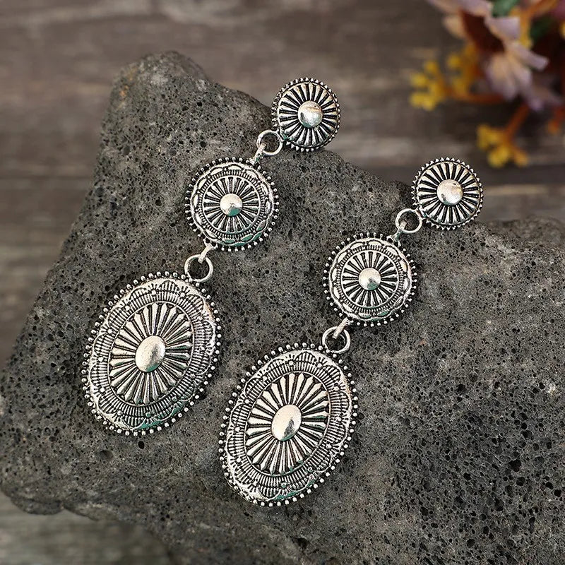 Silver sunburst drop earrings with oval and round embossed details.