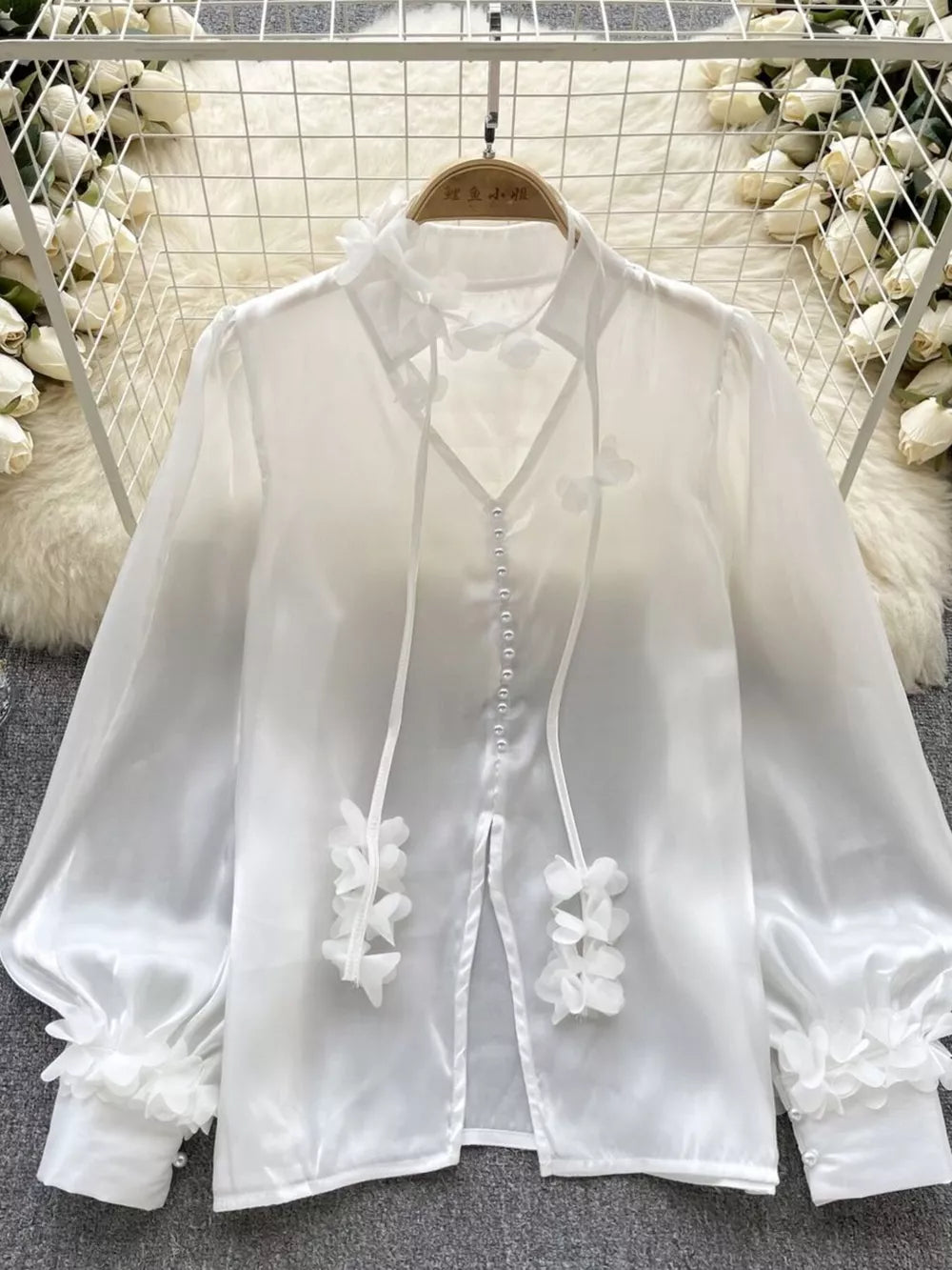 White sheer button-down shirt with delicate floral appliqué and bow details.