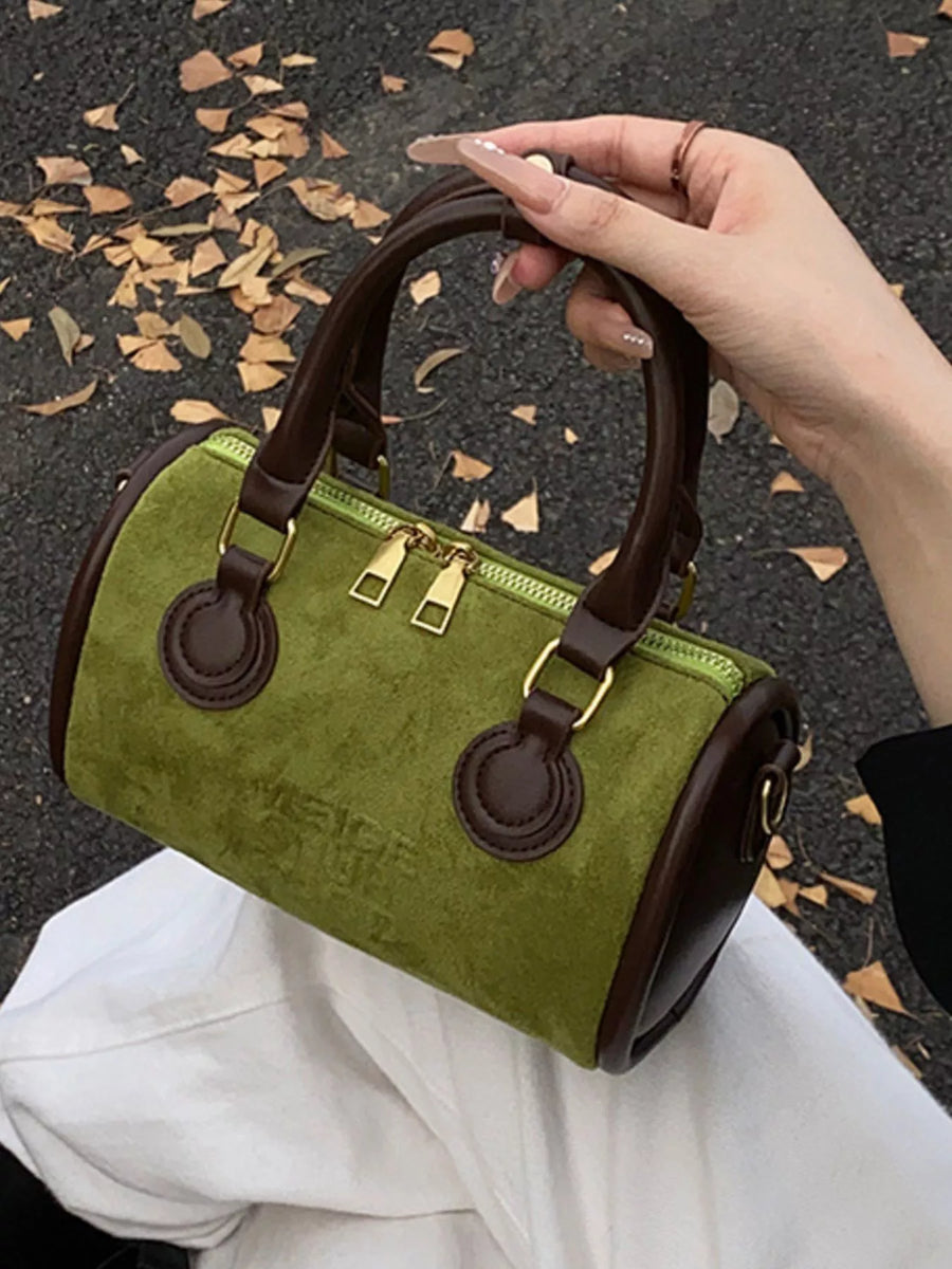 Green barrel crossbody bag with brown trim and gold hardware, held by a hand.