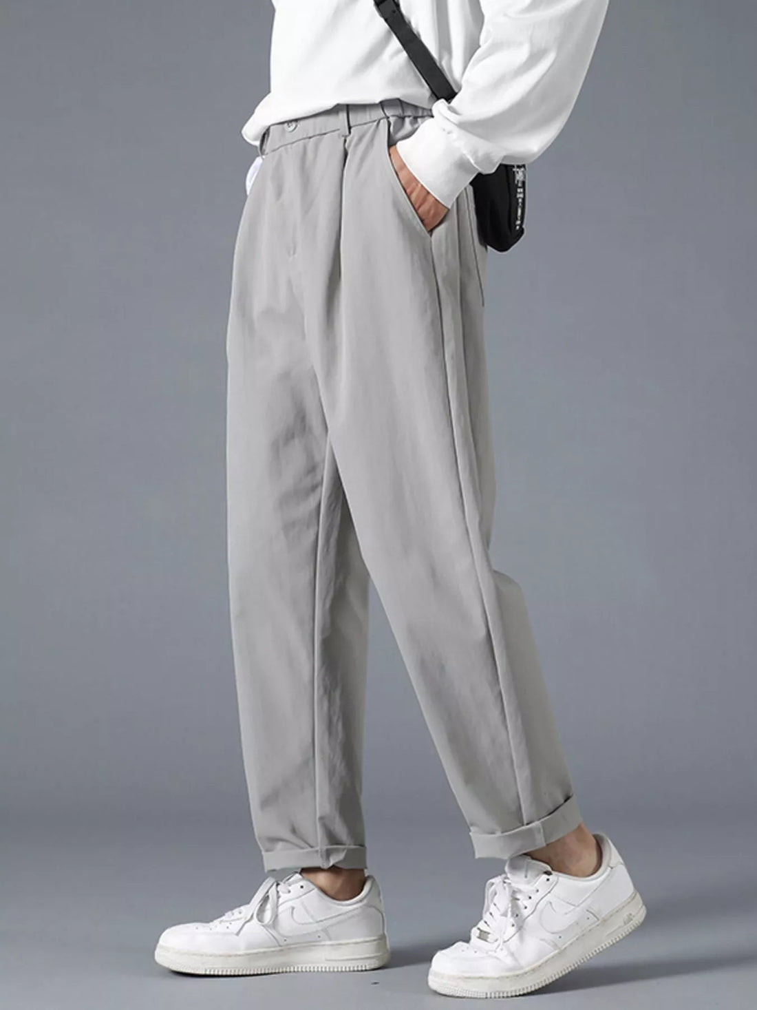 Grey casual loose fit pleated trousers with cuffed hems, styled with a white shirt and sneakers.