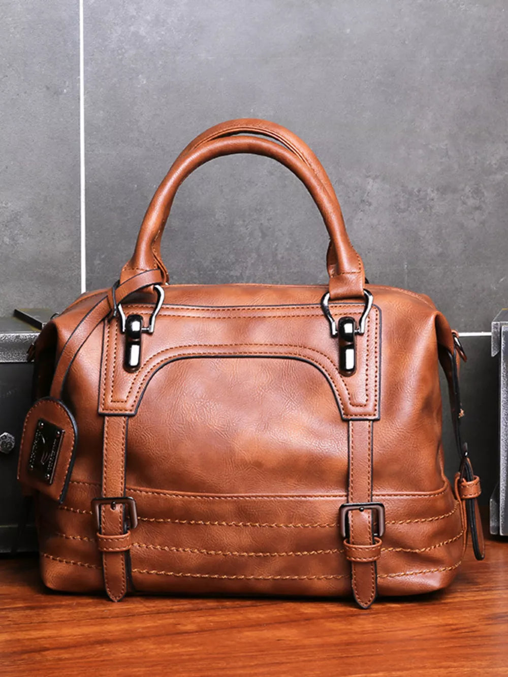 Brown leather half-moon handbag with buckle details and top handles.