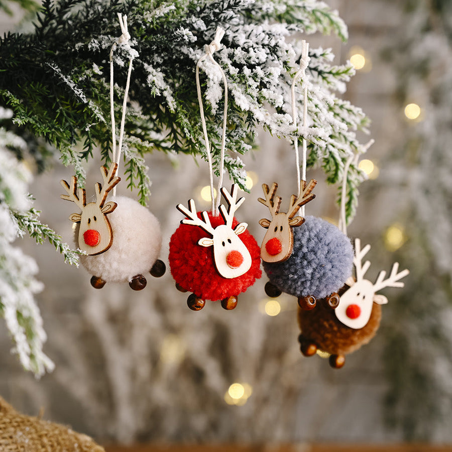 Four multicolor pom-pom reindeer ornaments with wooden antlers and red noses hang on a snowy branch.
