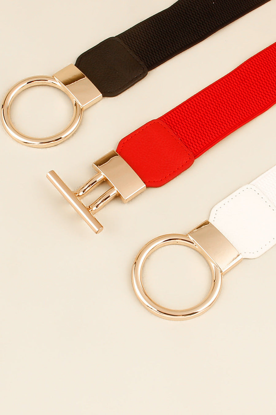 Elasticated ring buckle belts in black, red, and white with gold-tone hardware.