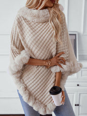 Beige knit poncho with faux fur trim and diamond pattern, styled with jeans and jewelry.