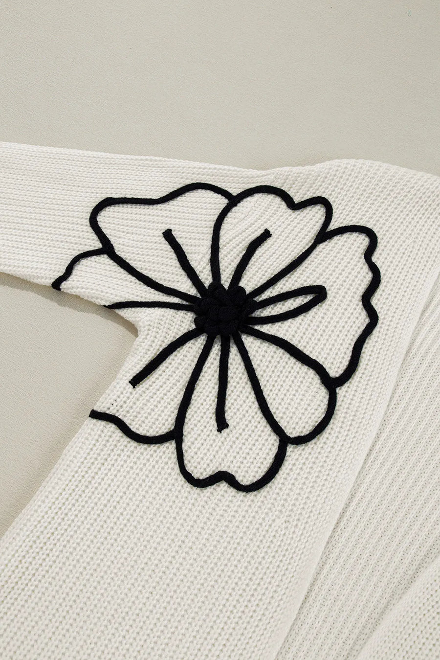 Ivory acrylic knit cardigan with black floral appliqué detail on sleeve