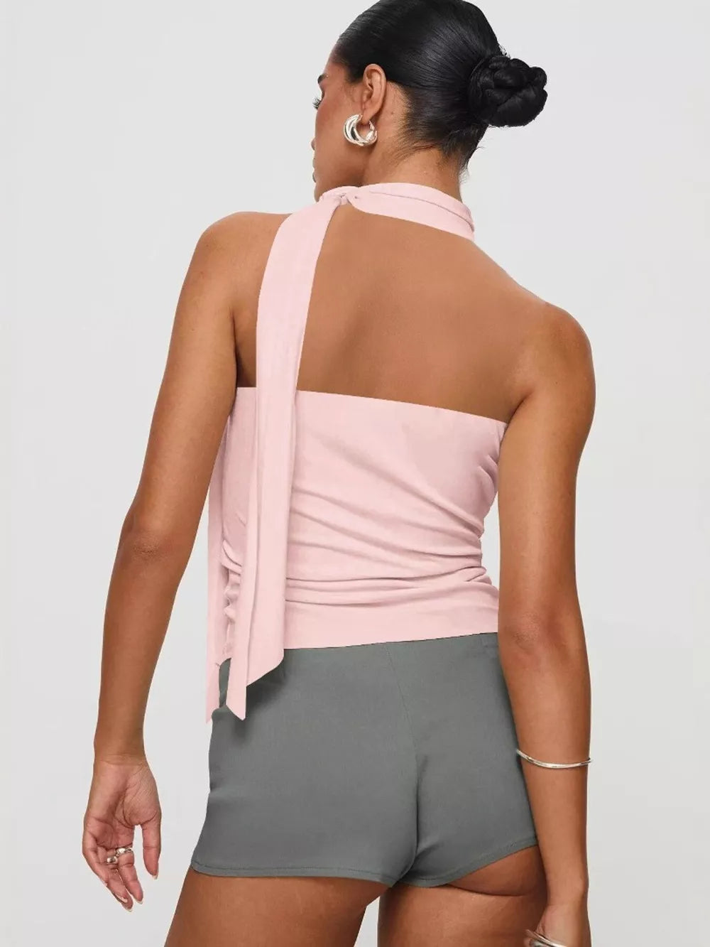 Pink halter top with draped tie detail and ruched sides, paired with grey shorts.