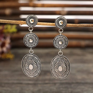 Silver sunburst drop earrings with layered circular and oval pendants.