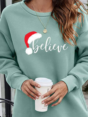 Sage Christmas graphic tunic sweatshirt with Santa hat and "believe" text.