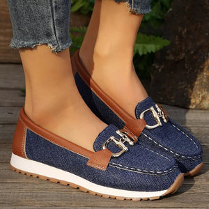 Blue denim slip-on loafers with brown trim and silver buckle detail.