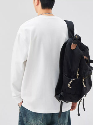 White casual oversized long-sleeve sweatshirt with crew neck, styled with jeans and a backpack.