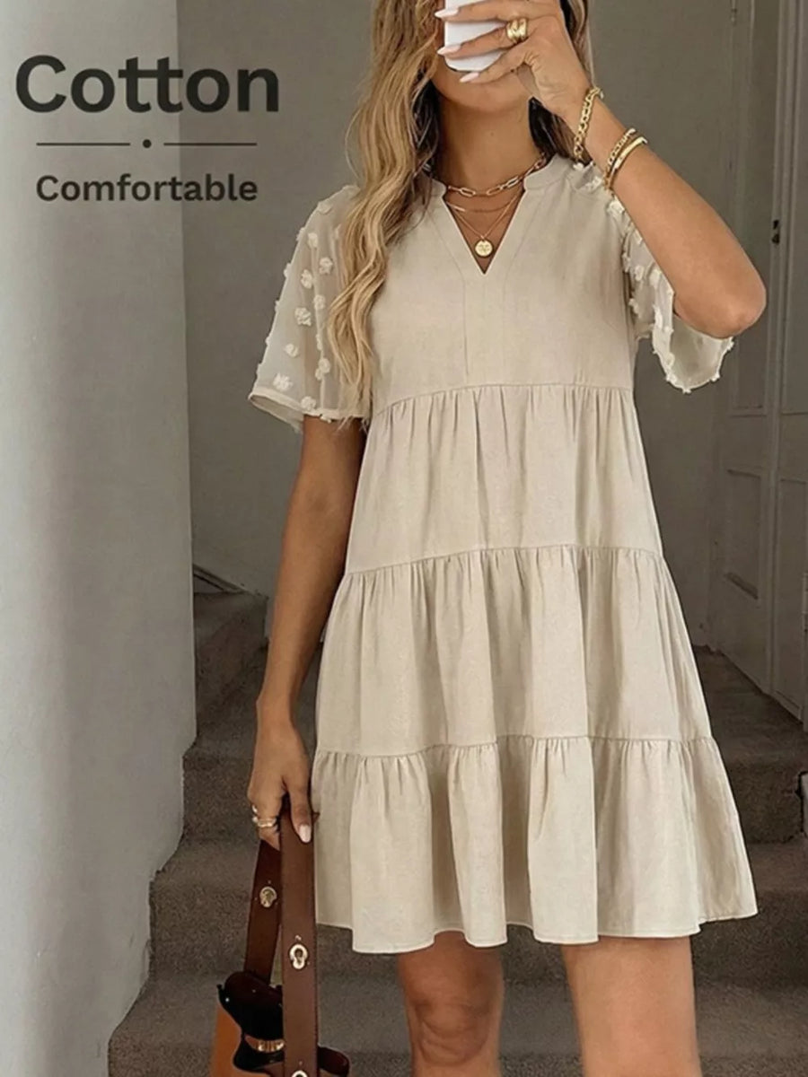 Beige cotton tiered mini dress with V-neck and sheer puff sleeves.
