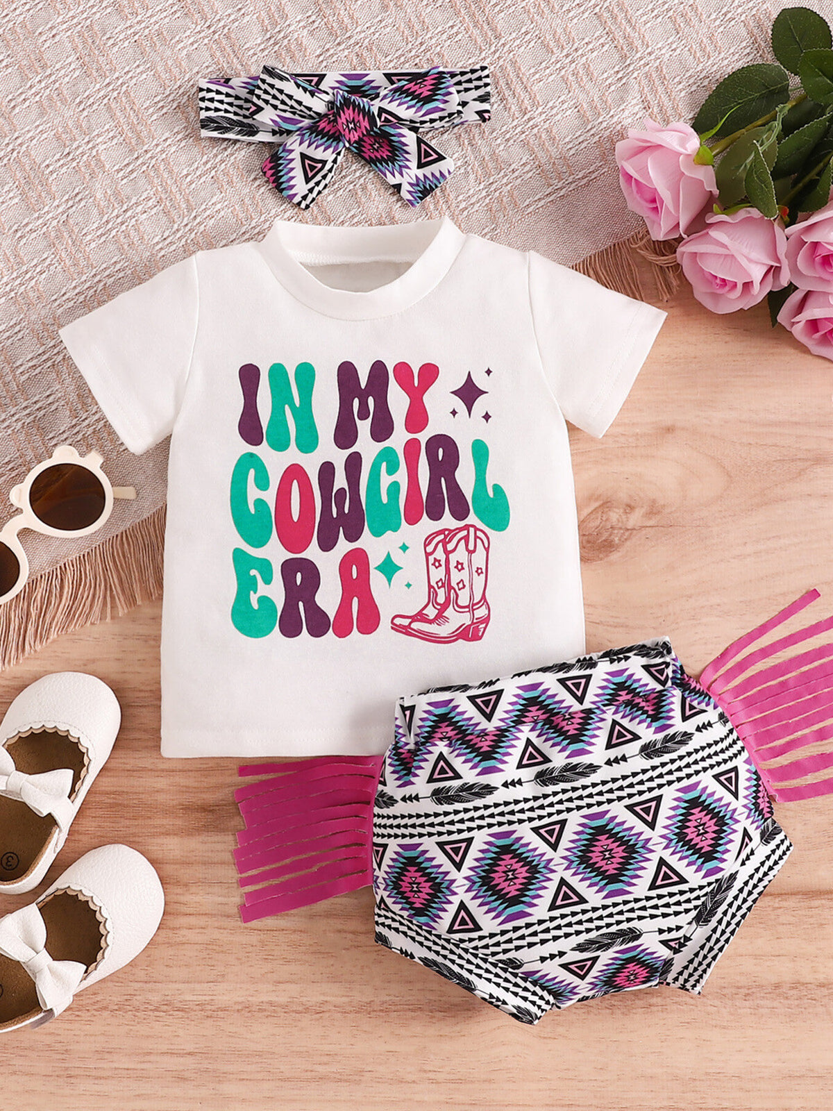 White baby graphic tee and fringe shorts set with cowgirl print and matching headband.