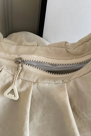 Beige gathered crescent shoulder bag with zipper detail and triangle pull tab