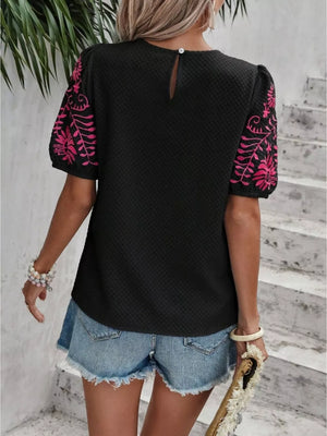 Black puff sleeve blouse with pink embroidery and textured fabric.