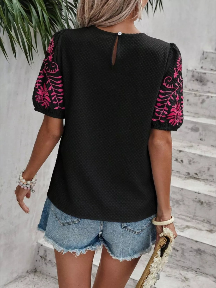 Black puff sleeve blouse with pink embroidery and textured fabric.