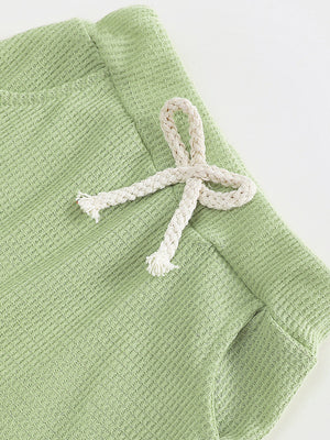 Green waffle knit children's pants with a decorative white drawstring bow.