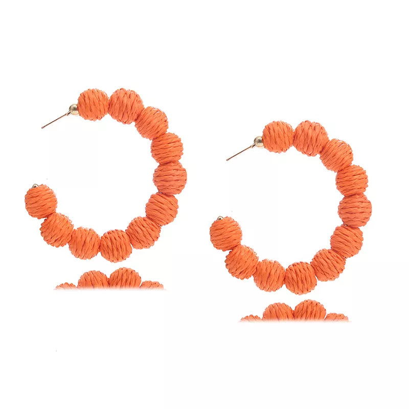 Orange raffia grass C-hoop earrings with textured ball details.