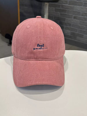 Pink baseball cap with embroidered "feel good" text in navy blue.