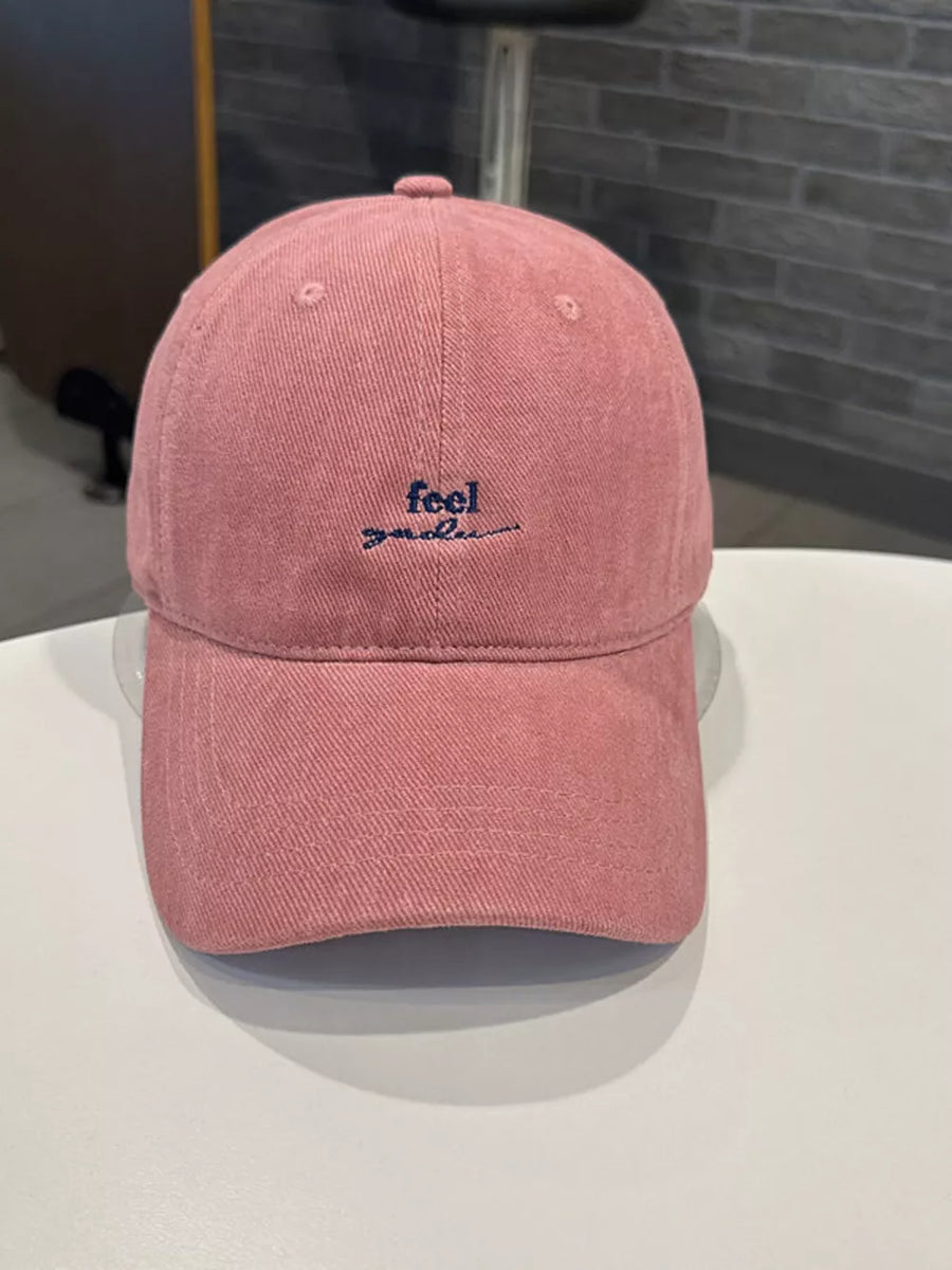 Pink baseball cap with embroidered "feel good" text in navy blue.