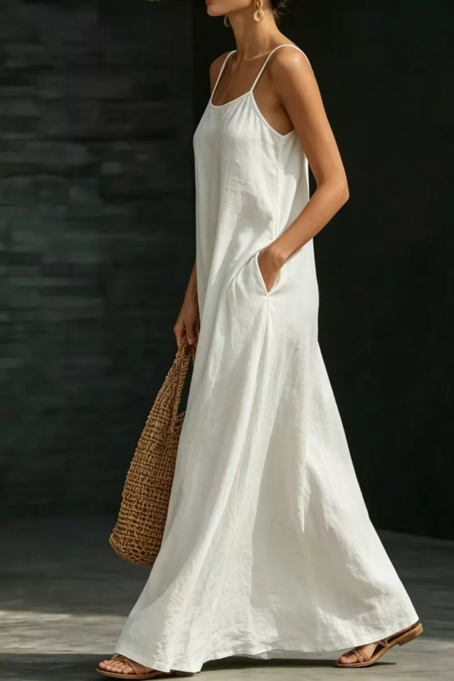 White A-line maxi dress with spaghetti straps and pockets, worn by a model with a straw bag.