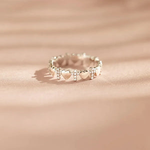 Sterling silver band ring with alternating heart and cross charms, accented with small stones.