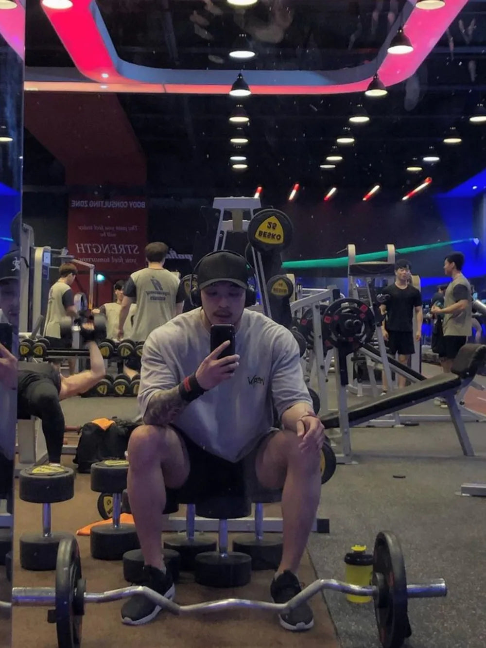 Oversized gray graphic tee with short sleeves and a crew neck, worn by a man in a gym.