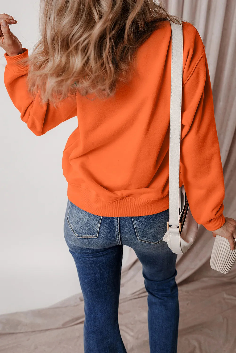 Orange graphic sweatshirt with crew neck and long sleeves, styled with jeans.