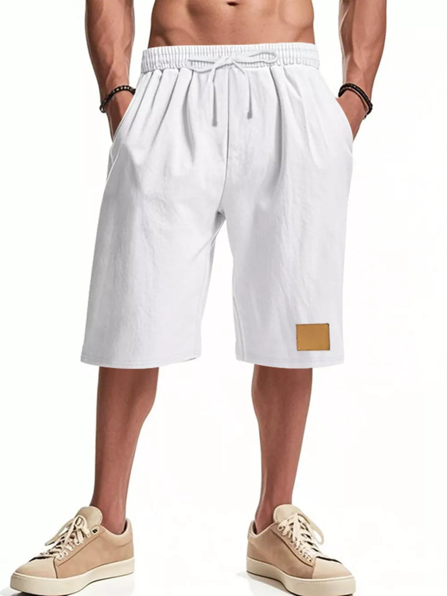 White chino shorts with drawstring waist and a leather patch detail, styled casually.