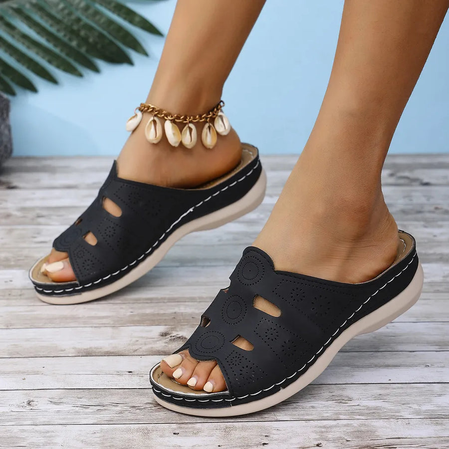 Black laser-cut comfort slide sandals with white stitching and a cushioned sole.