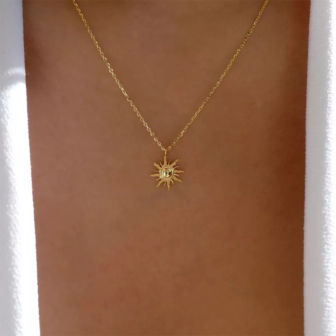 Gold sunburst pendant necklace with lace trim detail on a delicate chain.