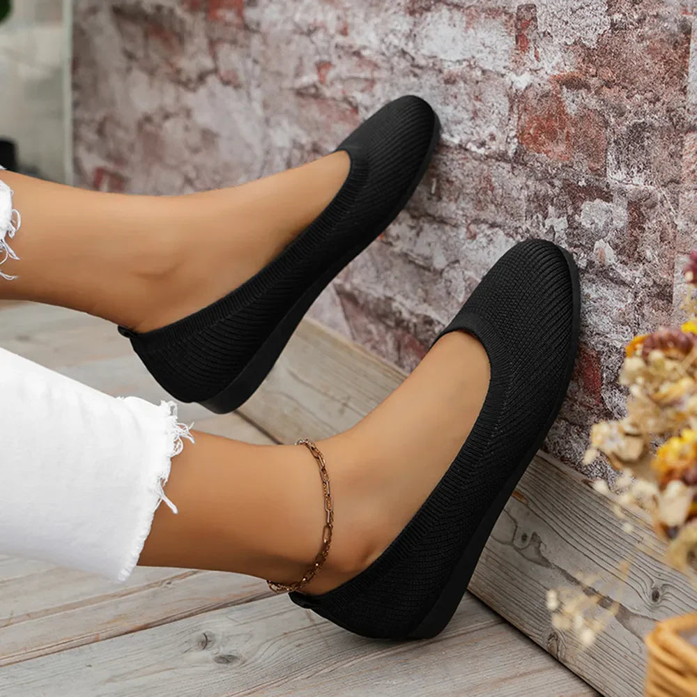 Black textured knit slip-on ballet flats with a round toe and a subtle ankle chain.