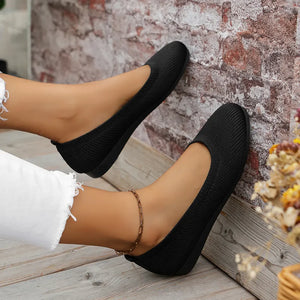 Black textured knit slip-on ballet flats with a round toe and a subtle ankle chain.