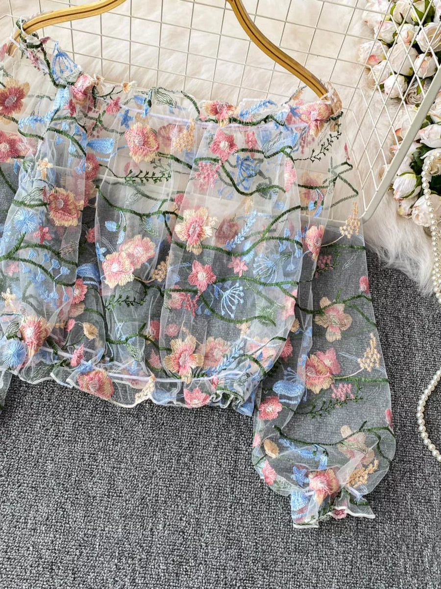 Embroidered floral off-shoulder t-shirt in sheer white with colorful blooms and green vines.