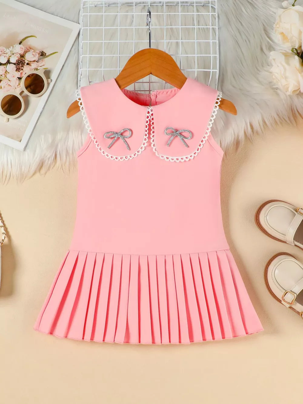 Pink toddler dress with Peter Pan collar, lace trim, two sparkly bows, and pleated skirt.
