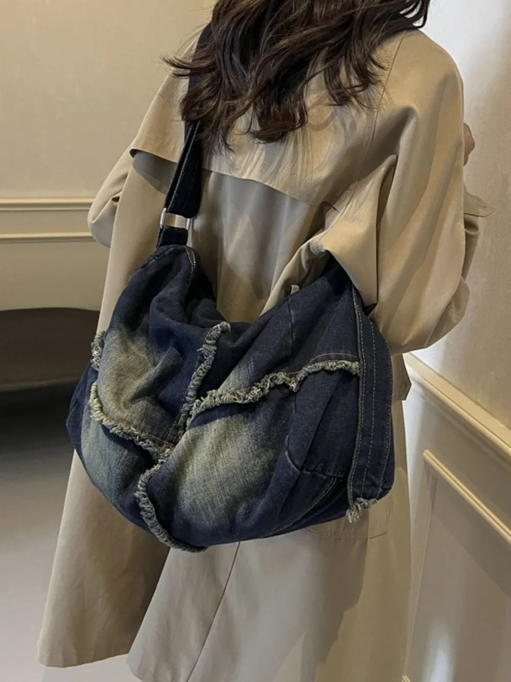 Frayed denim slouch crossbody bag in dark wash with distressed details.