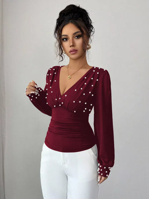 Burgundy ruched V-neck blouse with pearl embellishments and long sleeves.