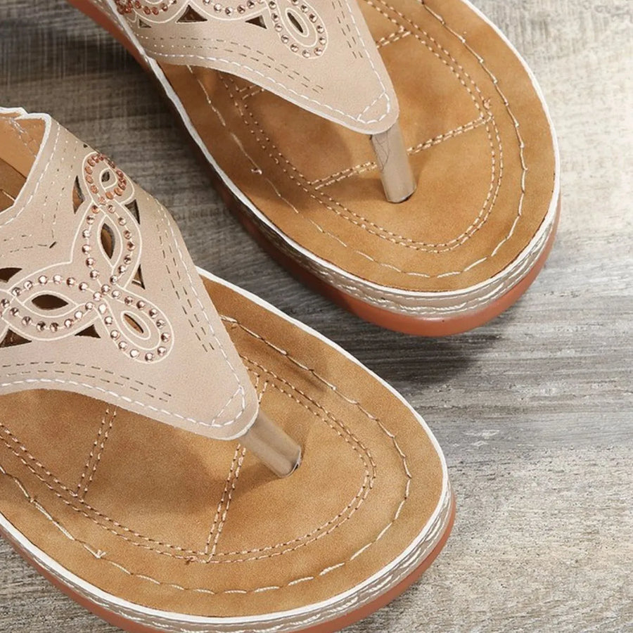 Beige laser-cut thong sandals with decorative rhinestones and stitching detail.