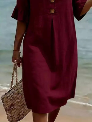 Burgundy ruffled sleeve dress with button detail and a woven tote bag on the beach.