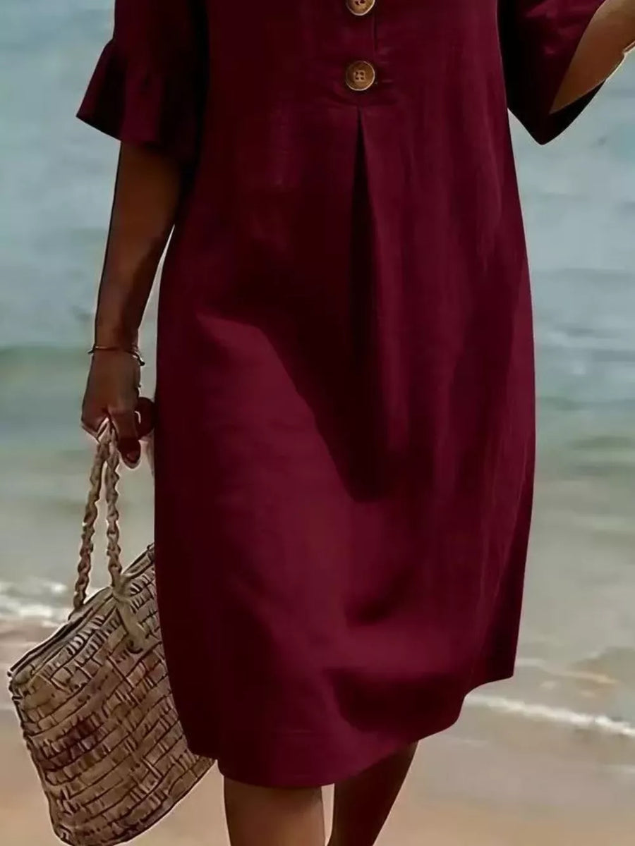 Burgundy ruffled sleeve dress with button detail and a woven tote bag on the beach.